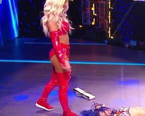 WWE - Carmella in red outfit standing over Sasha Banks